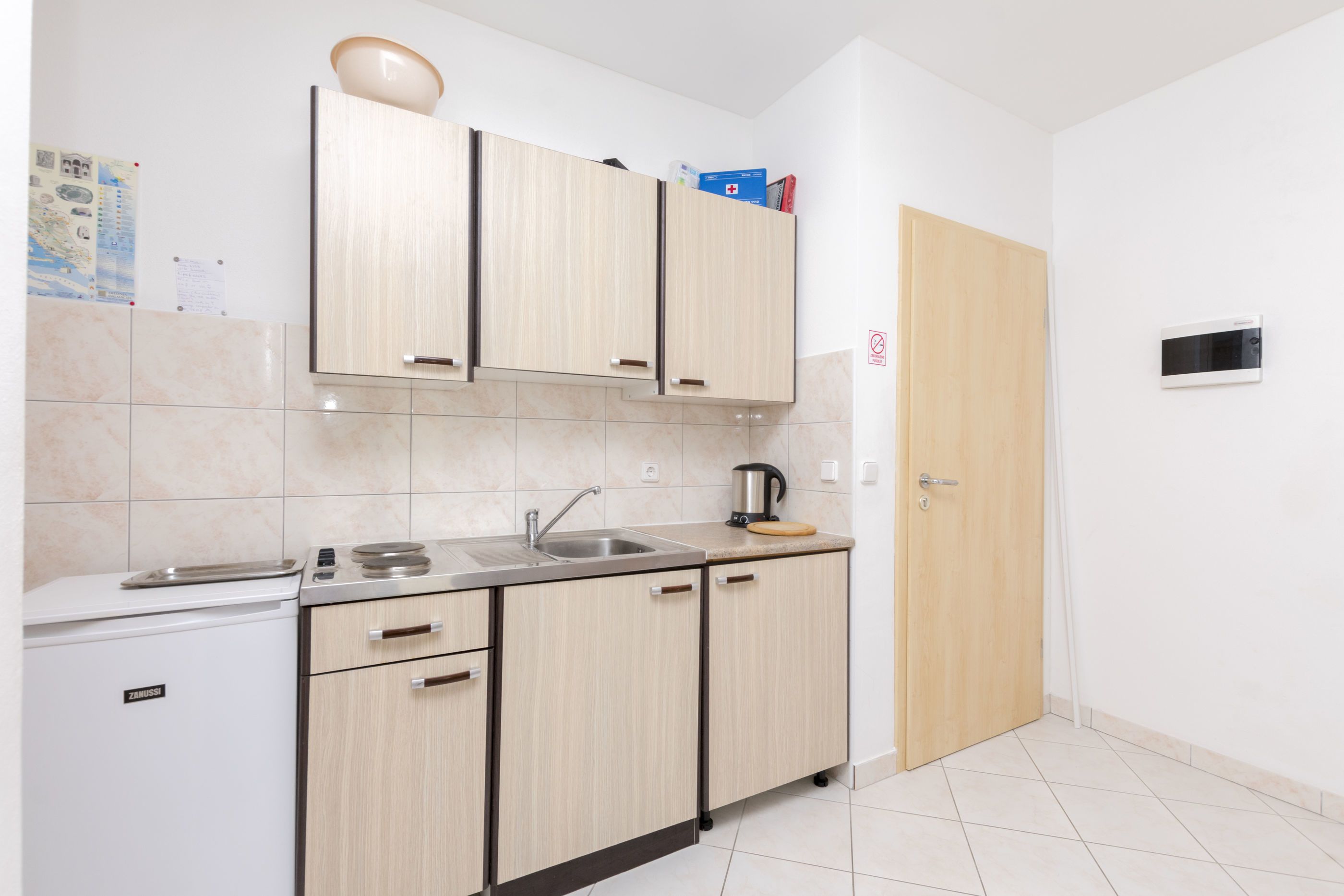 A compact kitchen with light wood cabinets, a built-in oven, a sink, and a microwave.