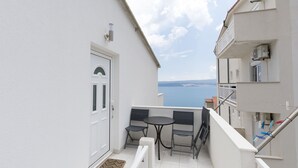 Ein Balkon mit zwei Stühlen und einem Tisch, eine weiße Tür und Blick aufs Meer.
