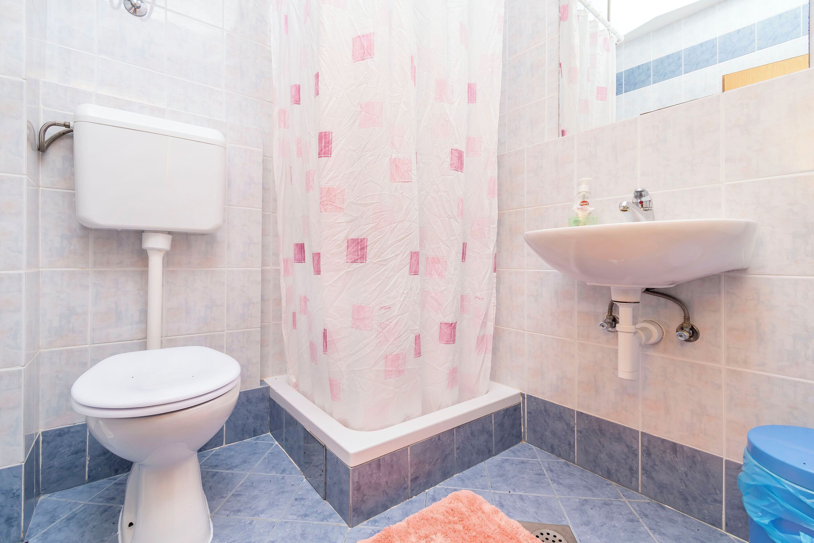 A bathroom with a toilet, shower curtain, sink, and blue-tiled floor.