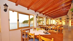 Un restaurant avec des tables et des chaises en bois, de grandes fenêtres donnant sur la mer et un plafond en bois.