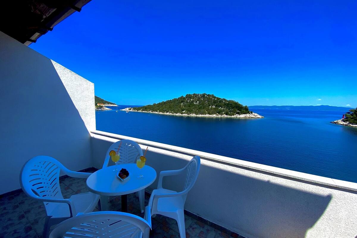 A balcony with a table and chairs overlooking a clear blue sea and a small island.