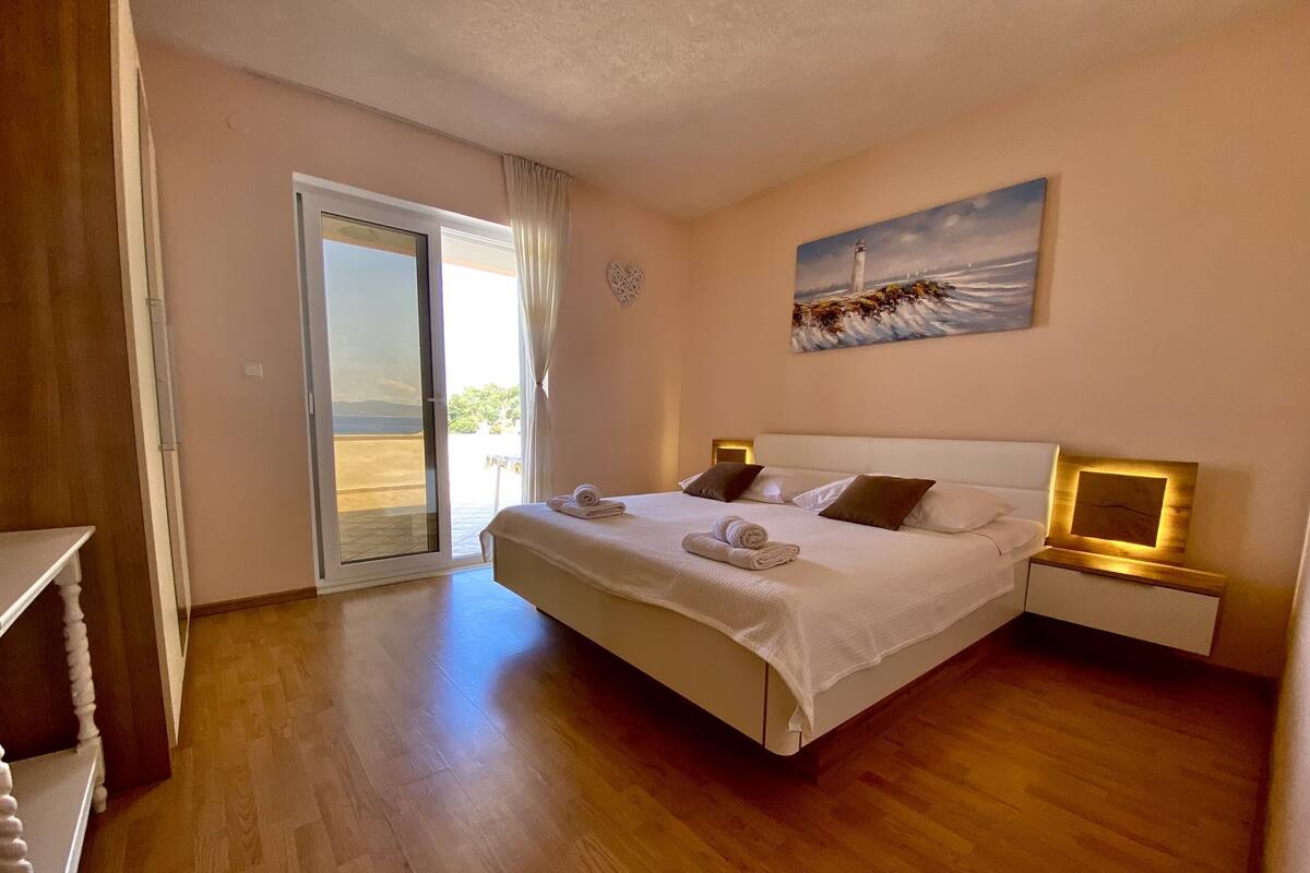 A hotel room with a large bed, a nightstand, a painting of a lighthouse, and a sliding glass door leading to an outdoor area.
