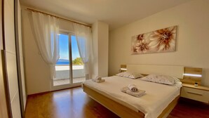 Une chambre avec un grand lit, une vue sur l’extérieur grâce à une porte-fenêtre coulissante et un tableau accroché au mur.
