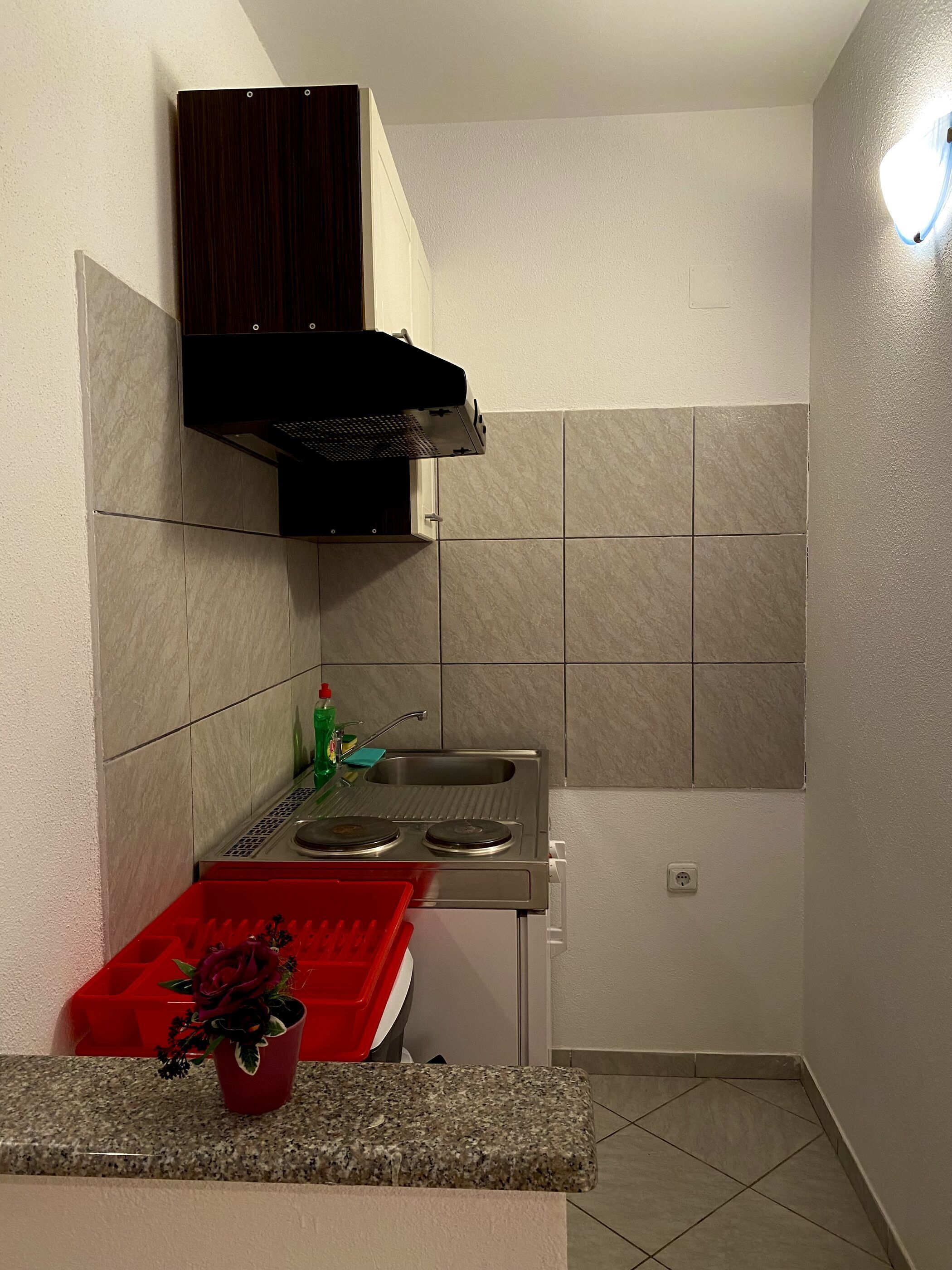 A compact kitchen with a stove, sink, and a red tray.
