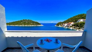 Un balcon avec une table et deux chaises, offrant une vue sur la côte, avec des bâtiments et de la végétation.