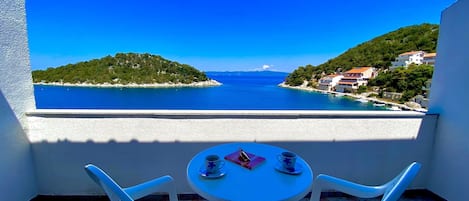 A balcony with a table and two chairs overlooking a coastal view with buildings and greenery.