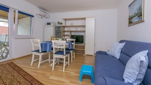 Ein Wohnzimmer mit einem blauen Sofa, einem Esstisch mit Stühlen und einem kleinen blauen Hocker.