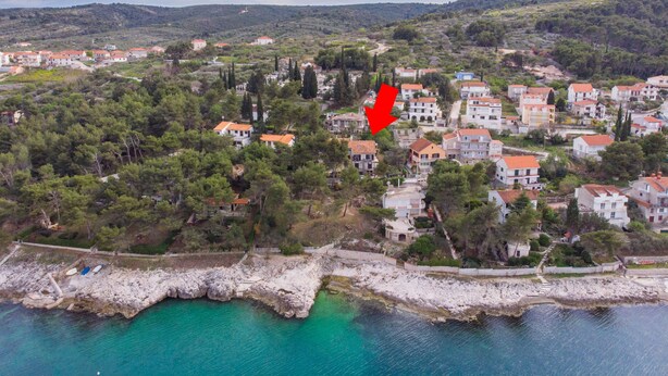 Vue aérienne d’un quartier résidentiel situé sur la côte, avec des maisons, des arbres et une côte rocheuse.