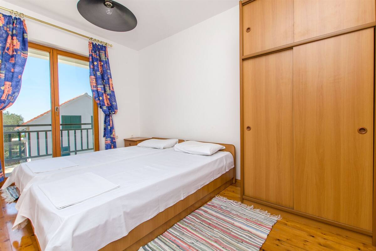 A bedroom with a bed, wooden wardrobe, and a balcony with curtains.