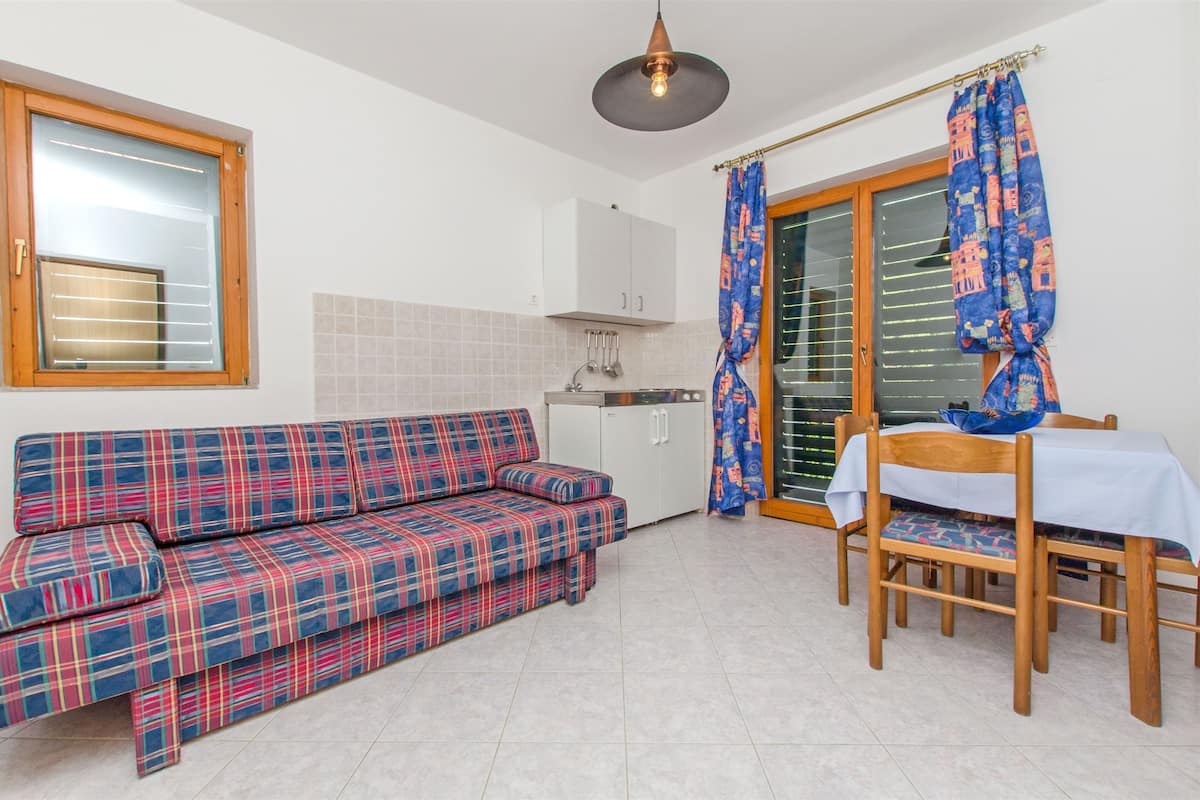 Une cuisine compacte dotée d’un four encastré, d’une table à manger avec des chaises et d’un canapé recouvert d’un plaid.