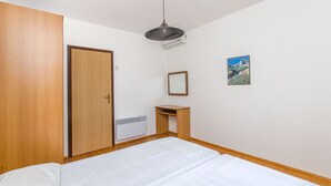 Une chambre à coucher comprenant un lit, une armoire en bois, un petit bureau, un miroir et un climatiseur fixé au mur.