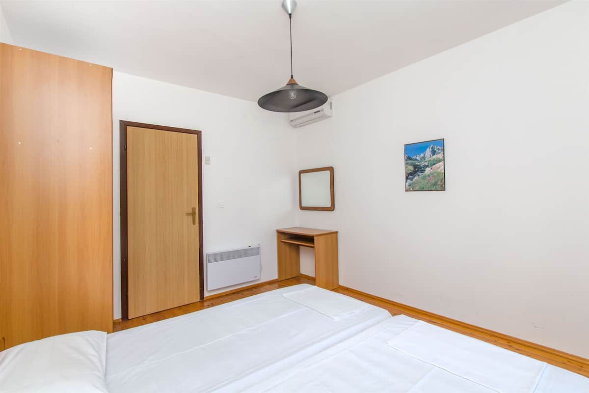 Une chambre à coucher comprenant un lit, une armoire en bois, un petit bureau, un miroir et un climatiseur fixé au mur.