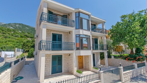 Un immeuble à plusieurs étages doté de balcons, d’un espace d’entrée pavé et d’une clôture qui l’entoure.