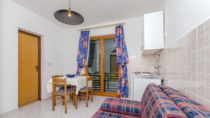 Un espace de vie compact comprenant une table à manger, des chaises, un canapé, un coin cuisine et une porte-fenêtre coulissante.