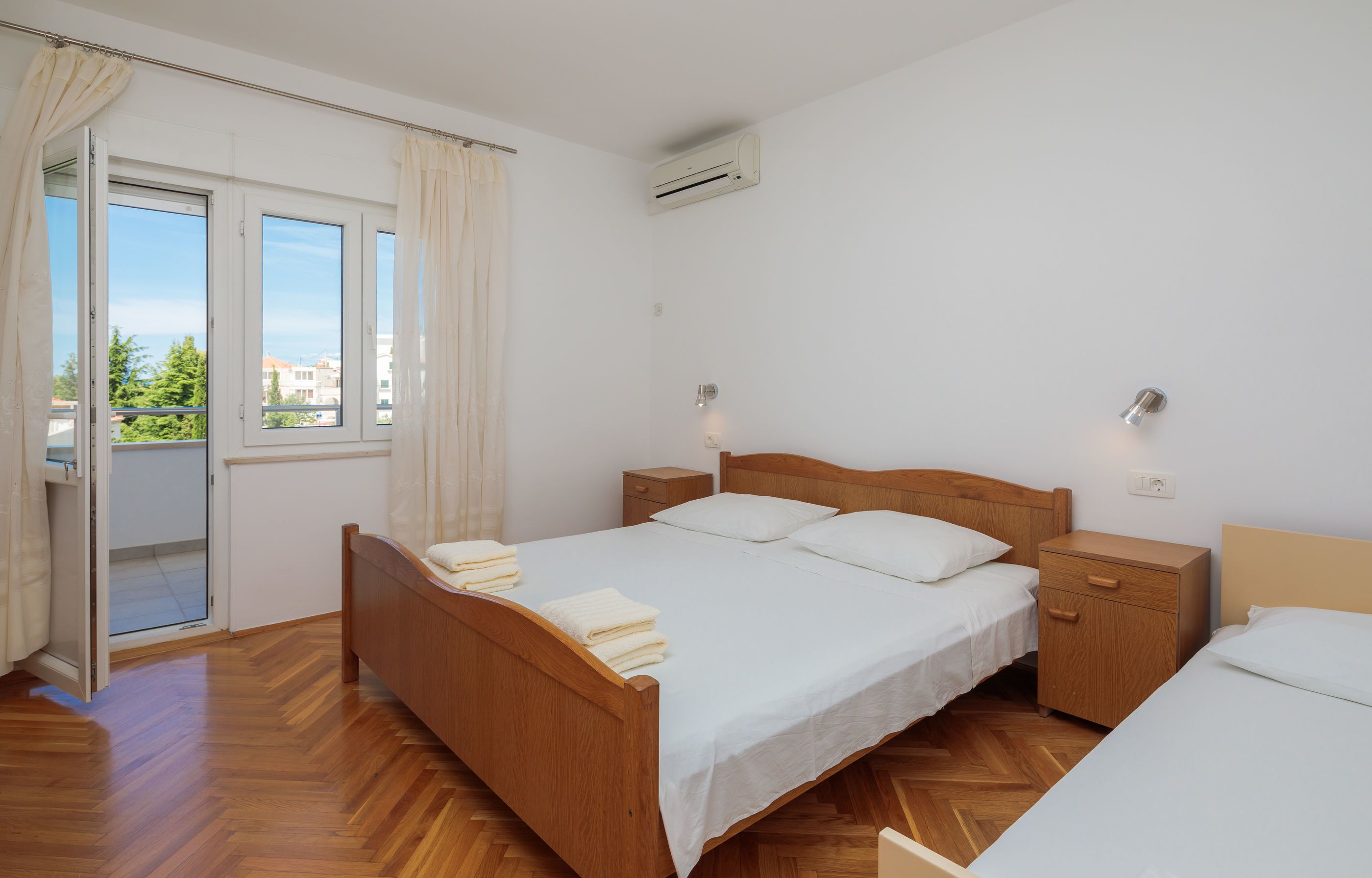 A bedroom with a wooden bed, a nightstand, a small wooden cabinet, and a window with curtains.