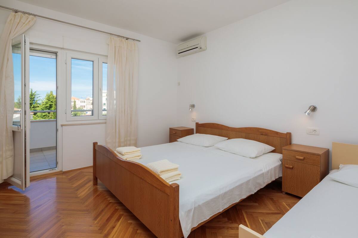 Un dormitorio con una cama de madera, una mesita de noche, un pequeño armario de madera y una ventana con cortinas.