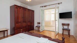 A bedroom with a large wardrobe, a bed, a TV, and a sliding glass door to a balcony. - Apartments and Rooms Denis (Duce)