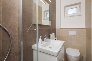 A modern bathroom with a glass shower enclosure, a white sink, and a toilet.