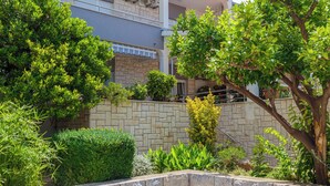 A landscaped garden with a stone wall, various shrubs, and a tree. - Apartments and Rooms Denis (Duce)