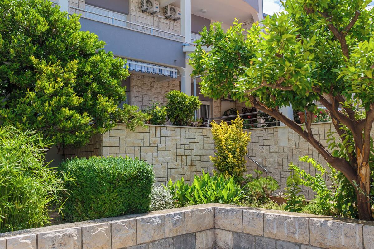 Un jardín ajardinado con un muro de piedra, diversos arbustos y un árbol.
