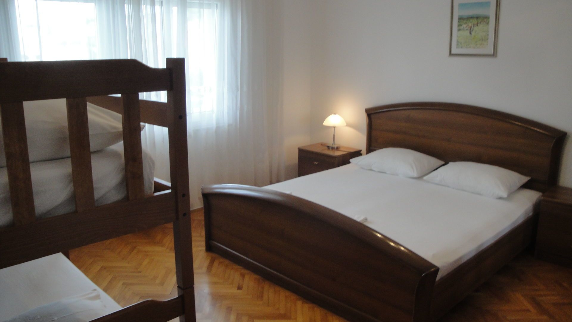 A wooden bed with white bedding in a room with a wooden floor and a nightstand with a lamp.