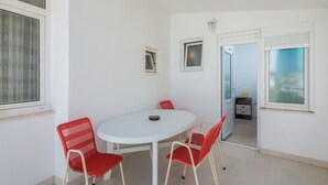 A small, white-walled room with a round table and four red chairs, a small window, and a door leading to another room. - Apartments and Rooms Denis (Duce)