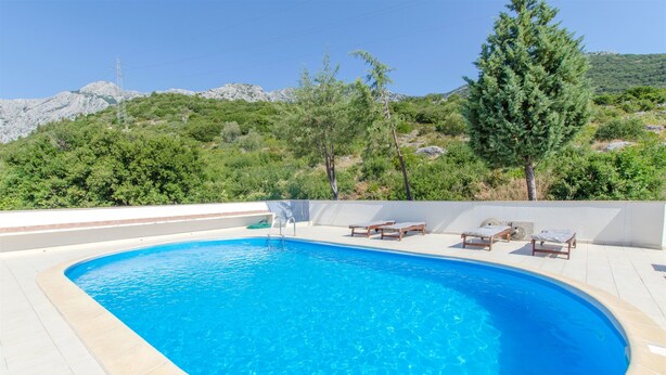 A swimming pool with a curved edge, surrounded by a tiled deck and wooden lounge chairs.