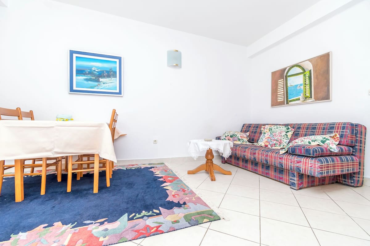 A living room with a dining table, a sofa, a rug, and wall art.