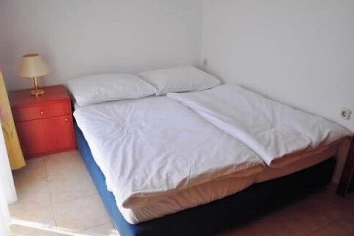 A single bed with white bedding in a room with white walls and a red nightstand.