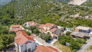 A residential area with houses featuring red-tiled roofs, surrounded by greenery and hills.