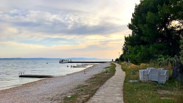 Ein Kiesstrand mit einem gepflasterten Weg, einem Steg und einem Stapel Reifen.