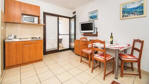 A compact kitchen with wooden cabinets, a microwave, and a dining area with a table and chairs. - Apartments Danica (Murter)