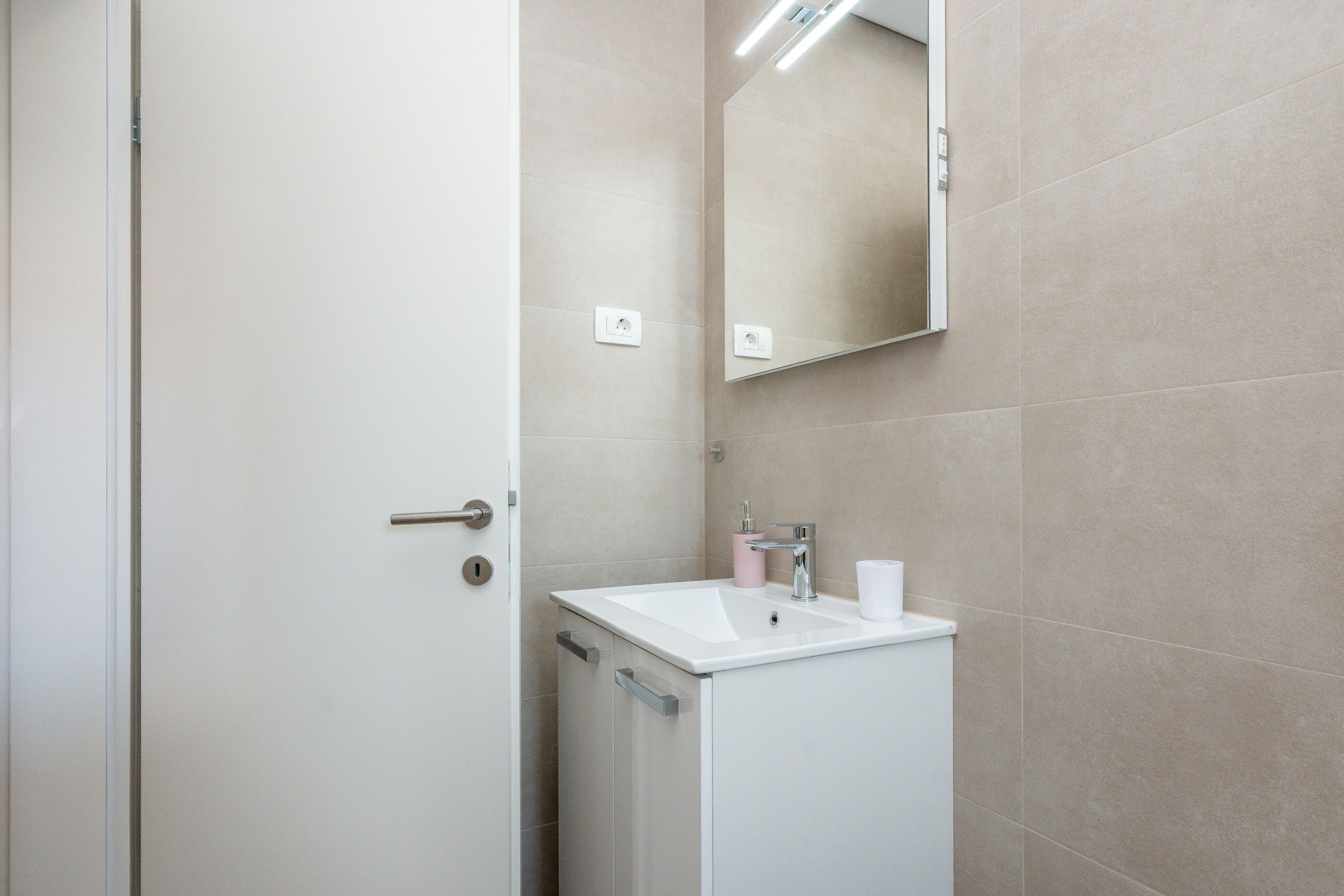 Ein Badezimmer mit einem weißen Waschbecken, einem Spiegel und einer Tür.