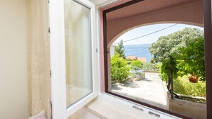 A room with a window overlooking a garden and a view of the sea. - Apartments Jozo (Stanici)