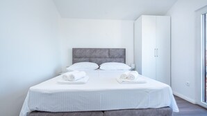 A modern hotel room with a large bed, grey headboard, white linens, and a wardrobe. - Apartments Jozo (Stanici)