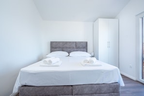 Ett modernt hotellrum med en stor säng, ett grått sänggavel, vita sängkläder och en garderob.