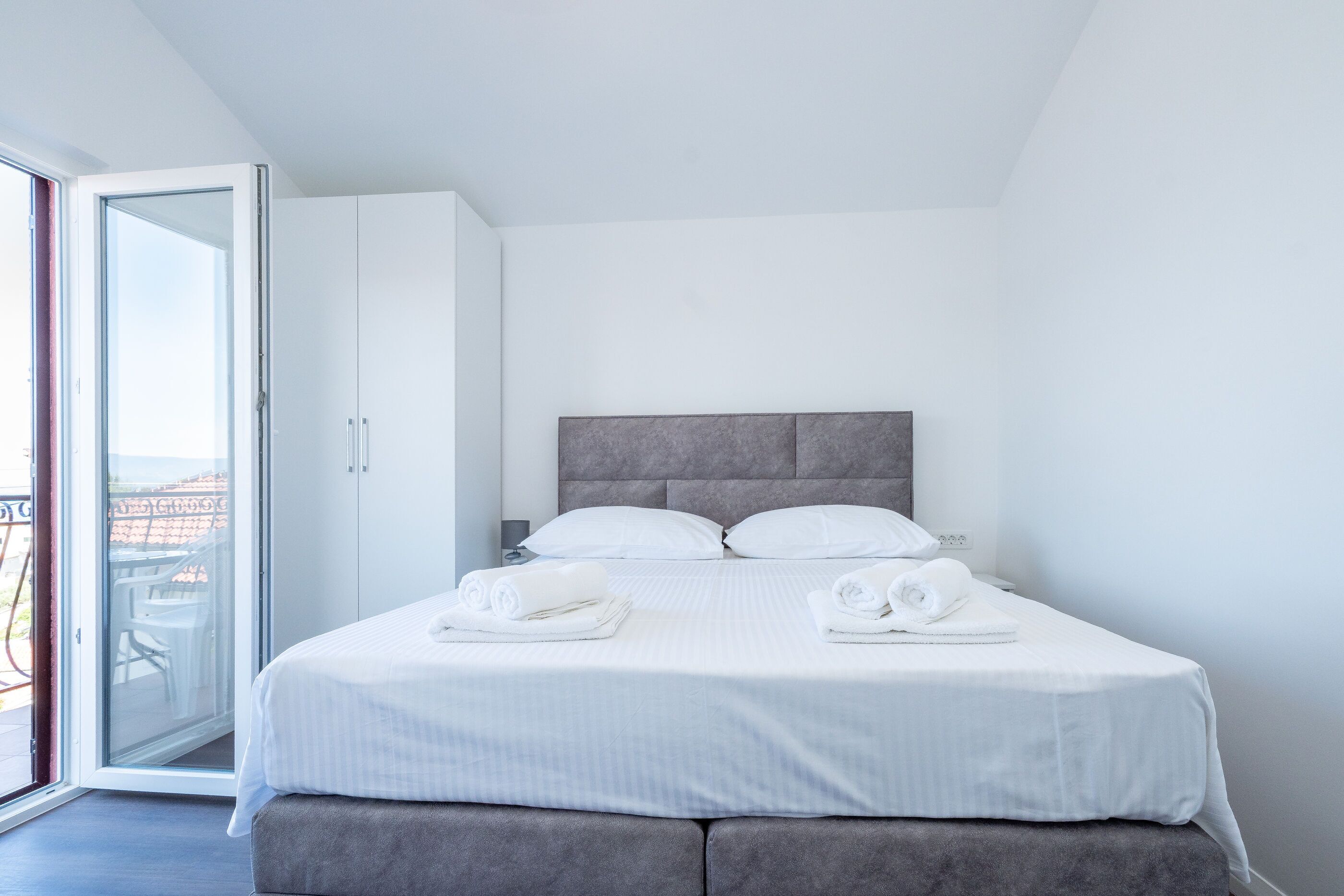 Une chambre moderne avec un lit, des oreillers et une vue sur l’extérieur, visible à travers une porte ouverte.