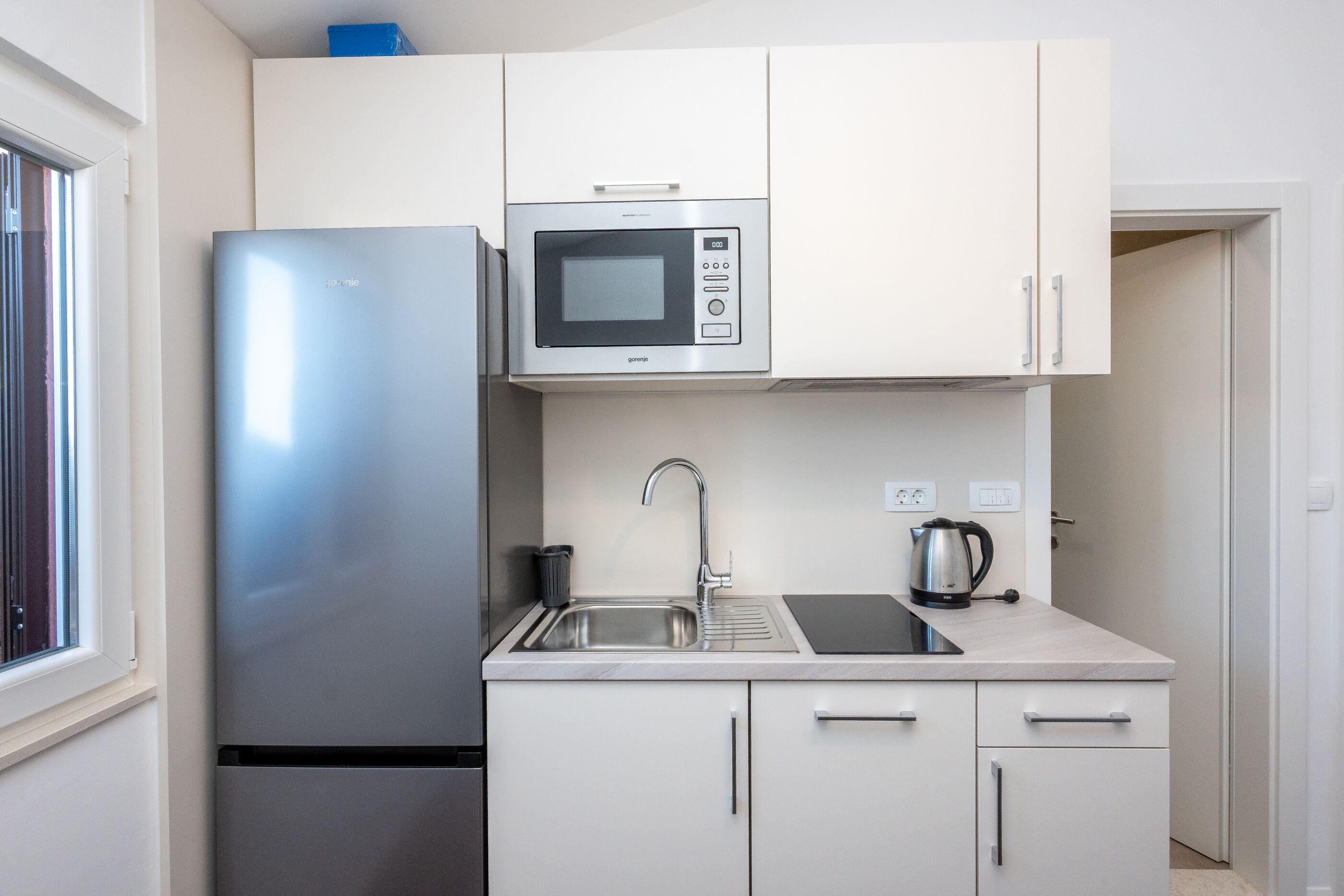 A compact kitchen with a refrigerator, microwave, sink, and cabinets.