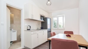 A modern kitchen with white cabinets, a microwave, and a refrigerator. There is a dining table with chairs and a bowl of fruit. - Apartments Jozo (Stanici)