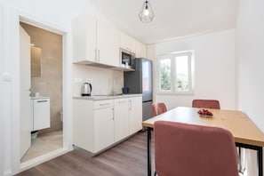 Una cocina moderna con armarios blancos, microondas y refrigerador. Hay una mesa de comedor con sillas y un tazón de fruta.