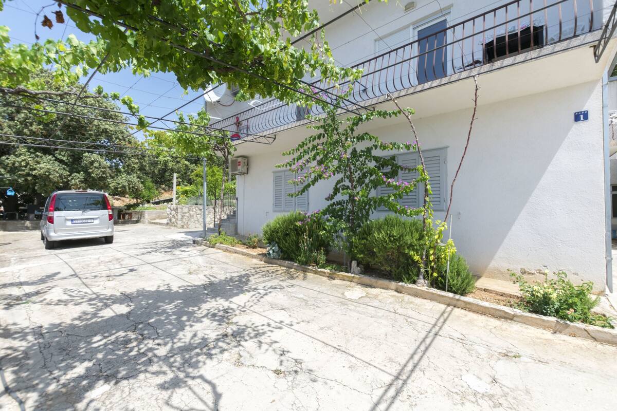 Une rue résidentielle avec un immeuble blanc, une voiture garée et un arbre aux feuilles vertes.