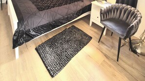 Une chambre à coucher comprenant un lit, une chaise, un bureau, une lampe, un ventilateur de plafond, une armoire et une fenêtre avec des rideaux.