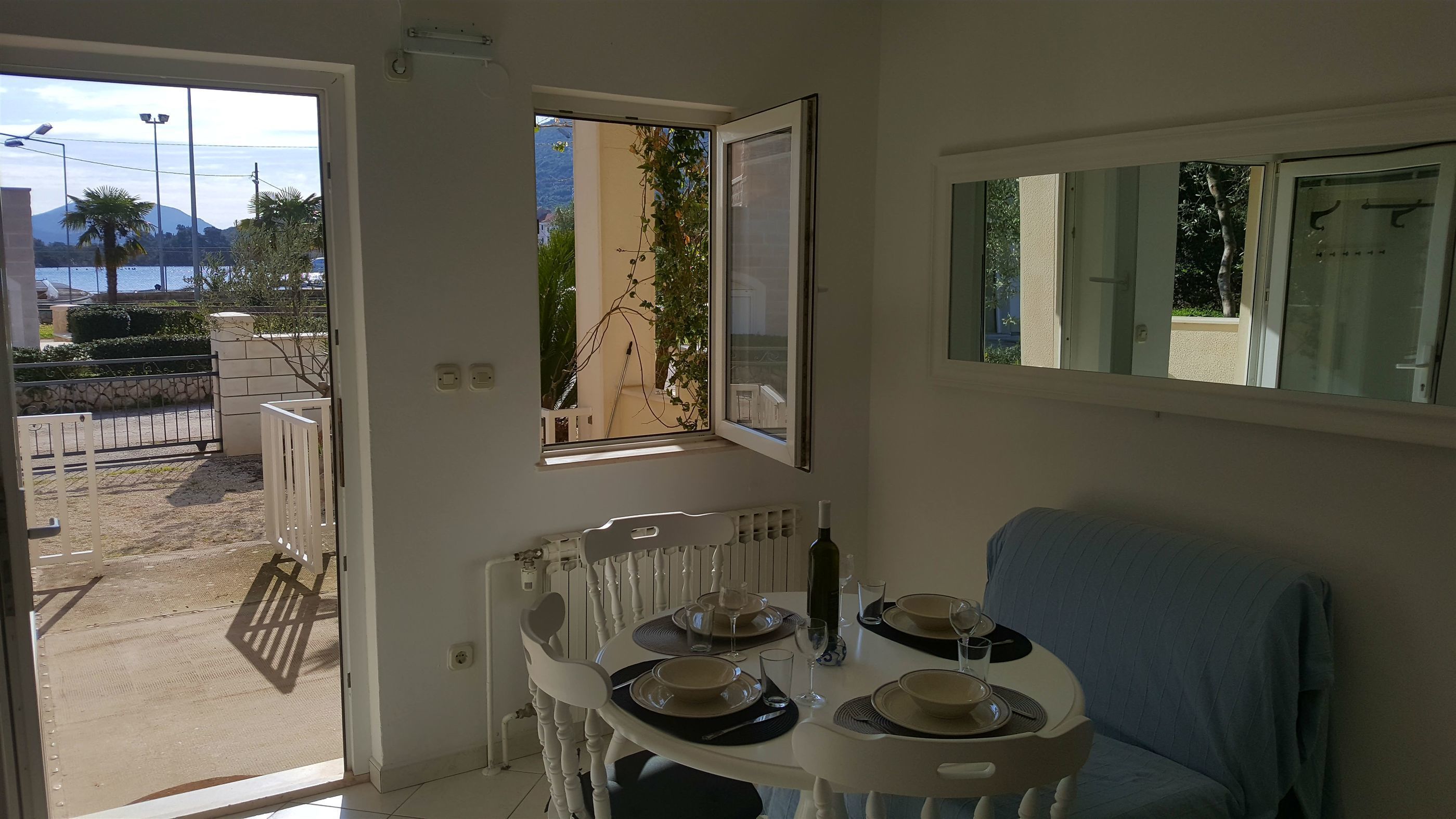 Un coin repas avec une table dressée pour deux personnes, un radiateur et une vue sur la montagne et la mer, visible par la fenêtre.