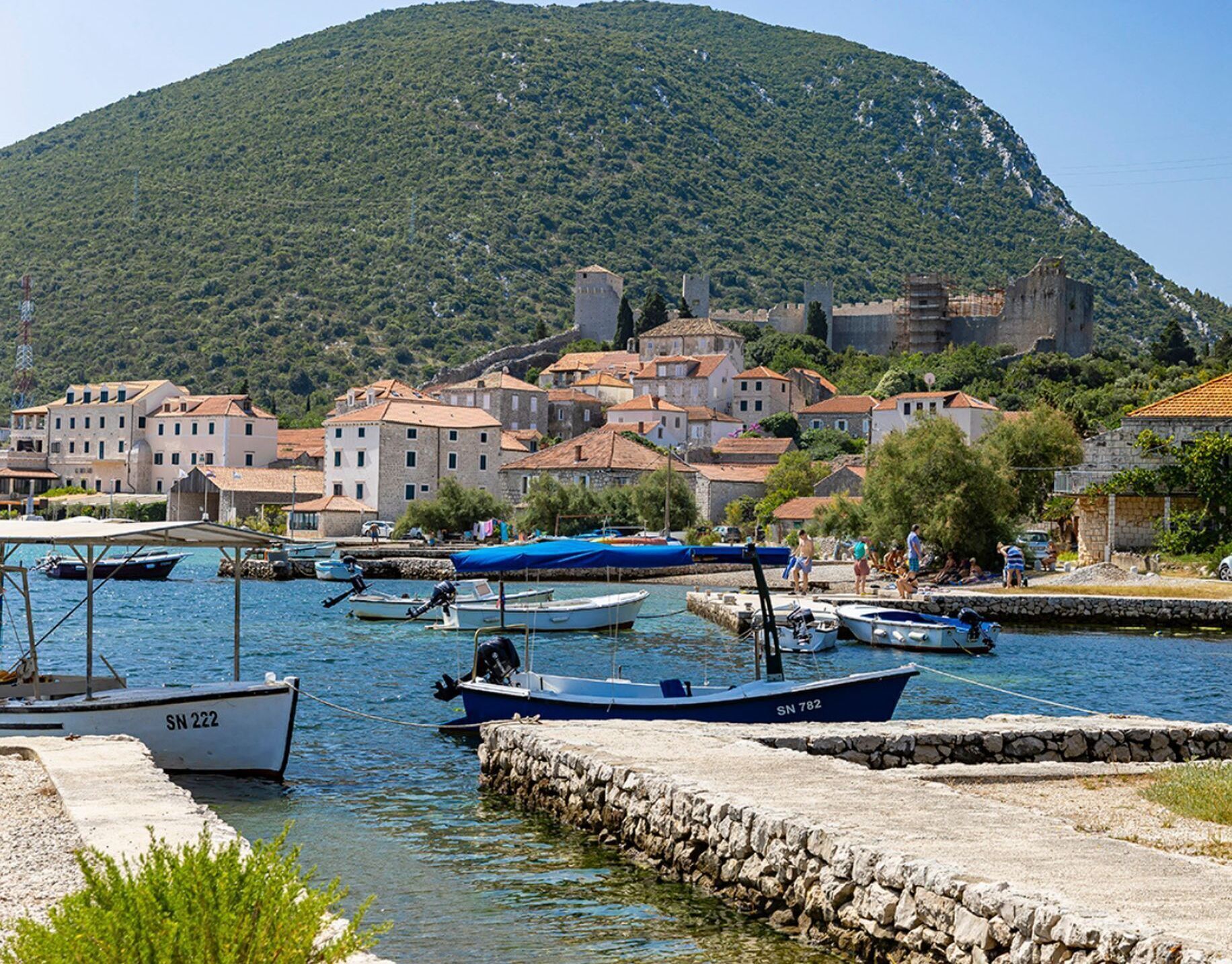 A coastal town with historic buildings, a stone wall, and boats docked at the harbor.