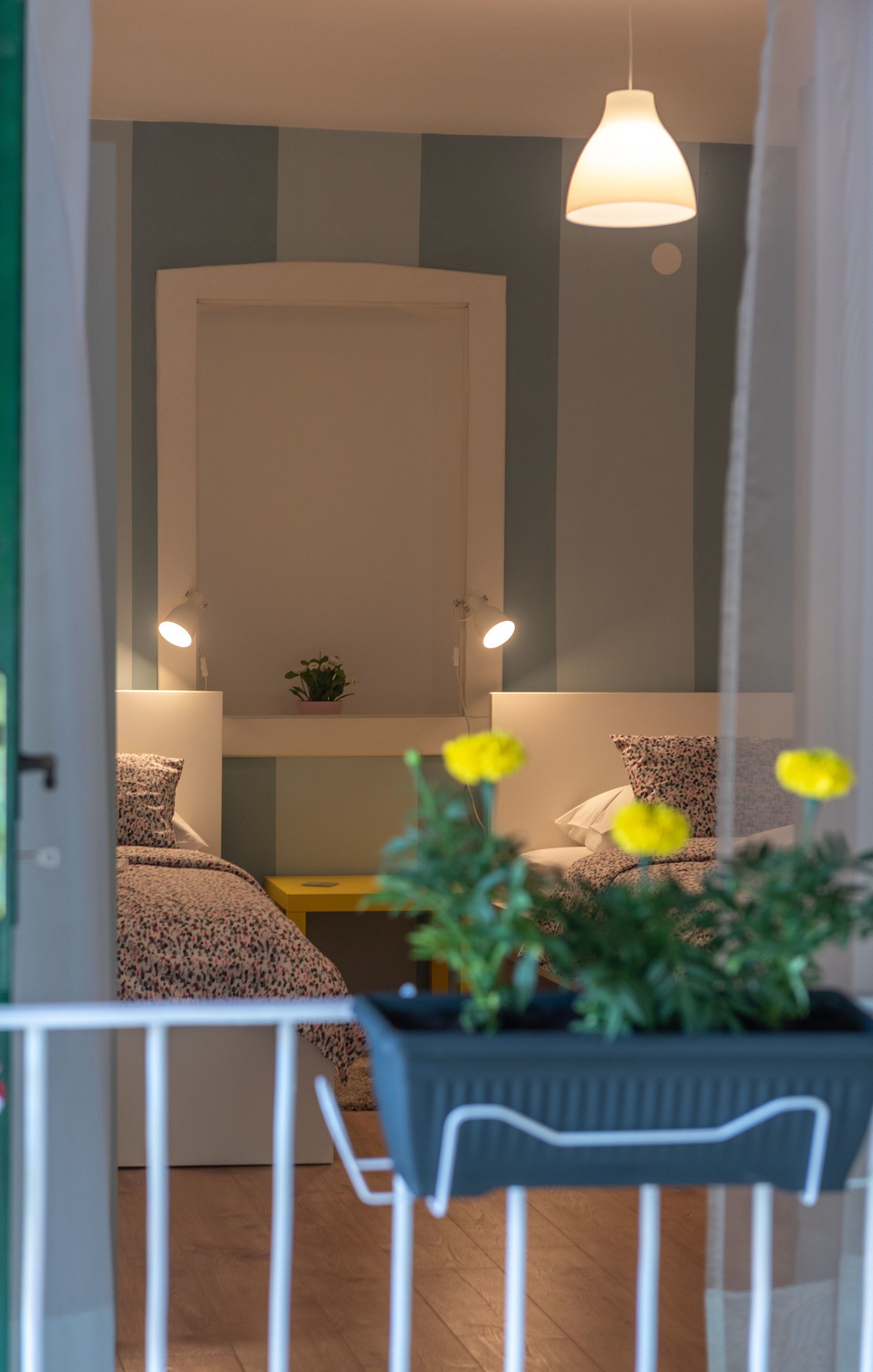 A bedroom with a bed, bedside lamps, a potted plant, and a hanging light fixture.