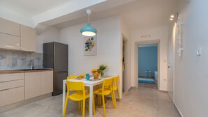 A modern kitchen with a dining area, featuring a stainless steel refrigerator, yellow chairs, and a blue pendant light. - House Polus (Trogir)