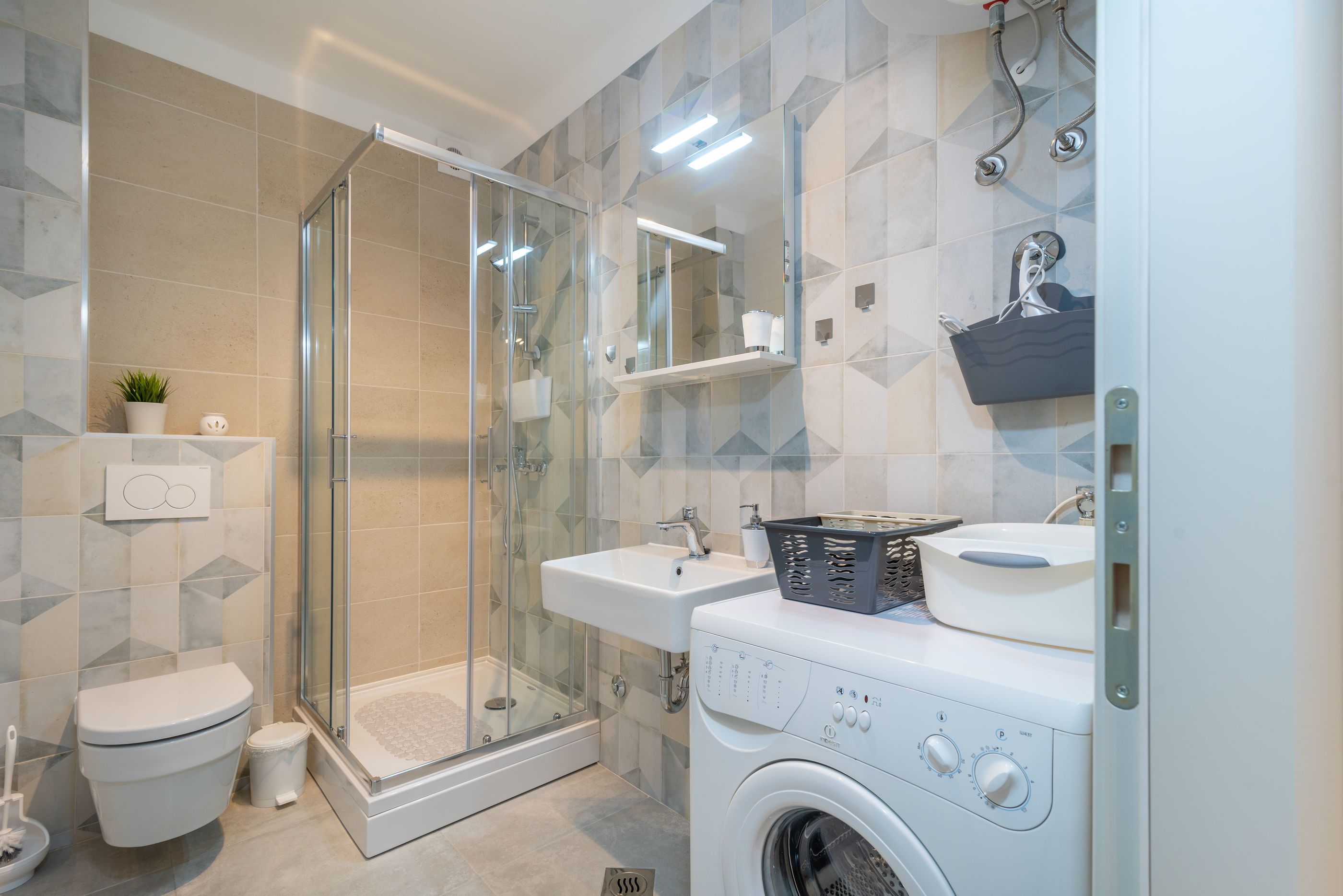 A modern bathroom with a glass shower enclosure, a toilet, a sink, and a washing machine.