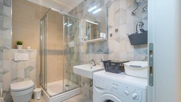 A modern bathroom with a glass shower enclosure, a toilet, a sink, and a washing machine.