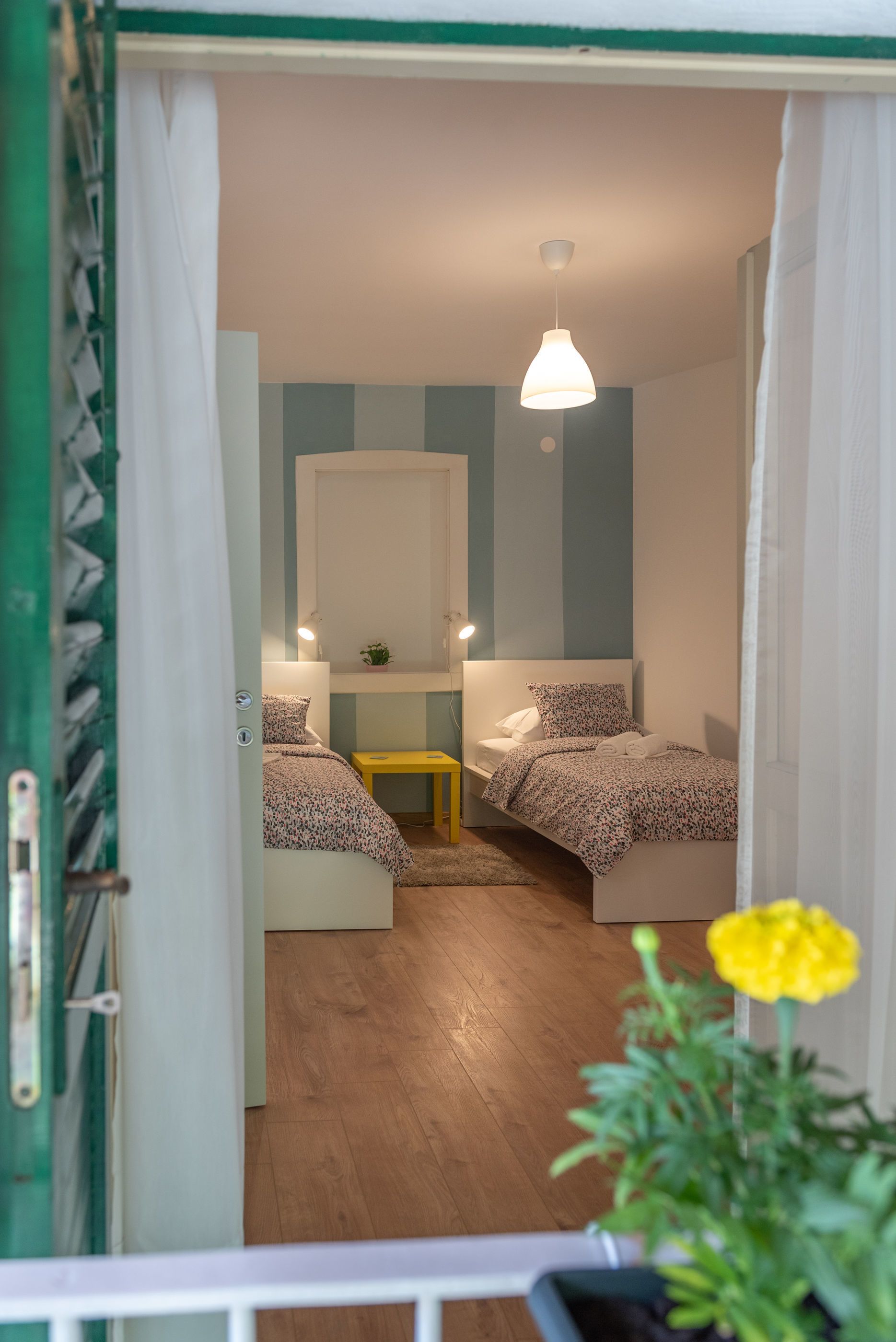 A bedroom with two beds, a bedside table, a mirror, and a hanging light fixture.