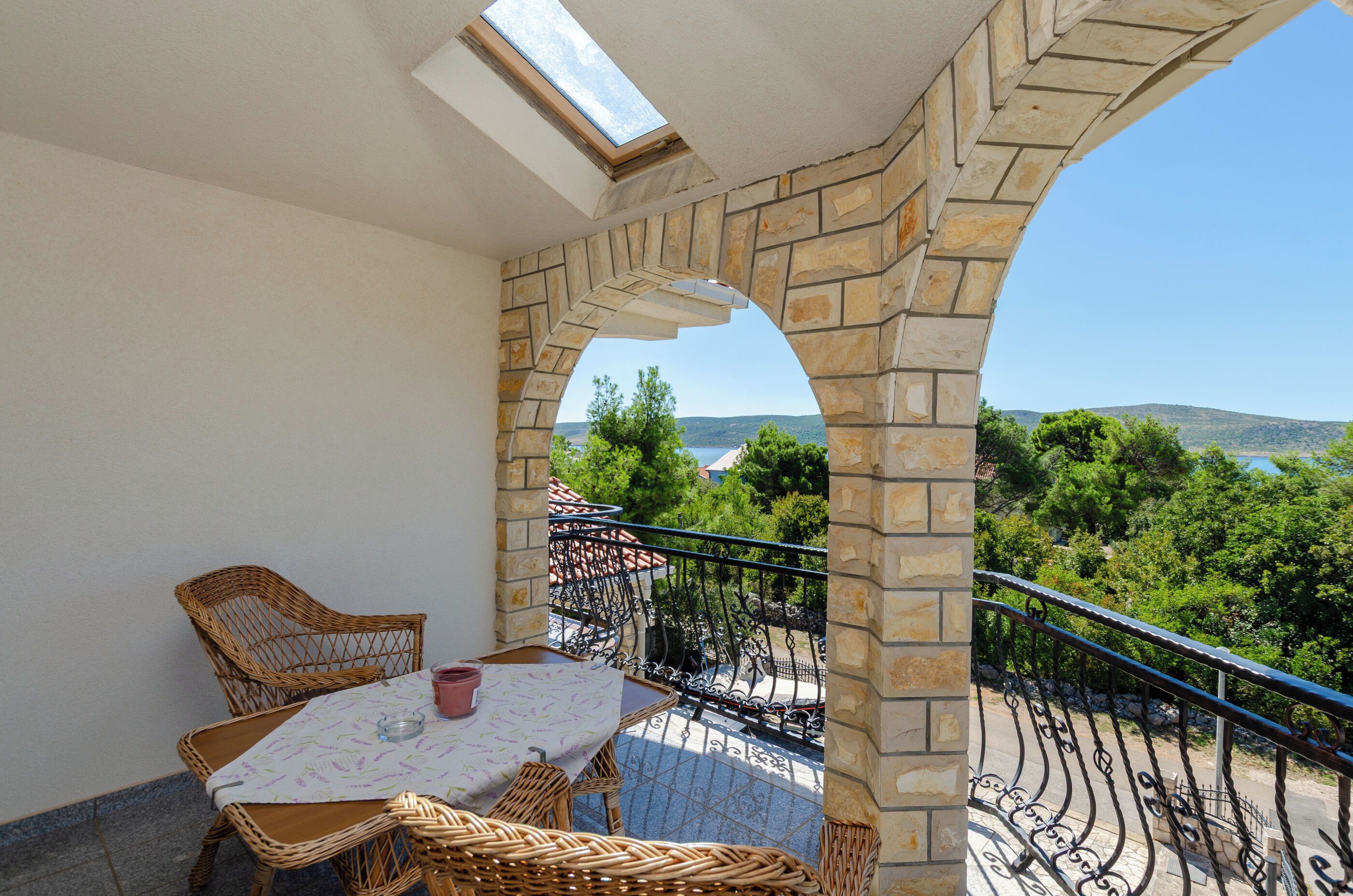 Ein Balkon mit Tisch und Stühlen, Blick auf Grünflächen und Hügel, sowie ein Steinbogen.